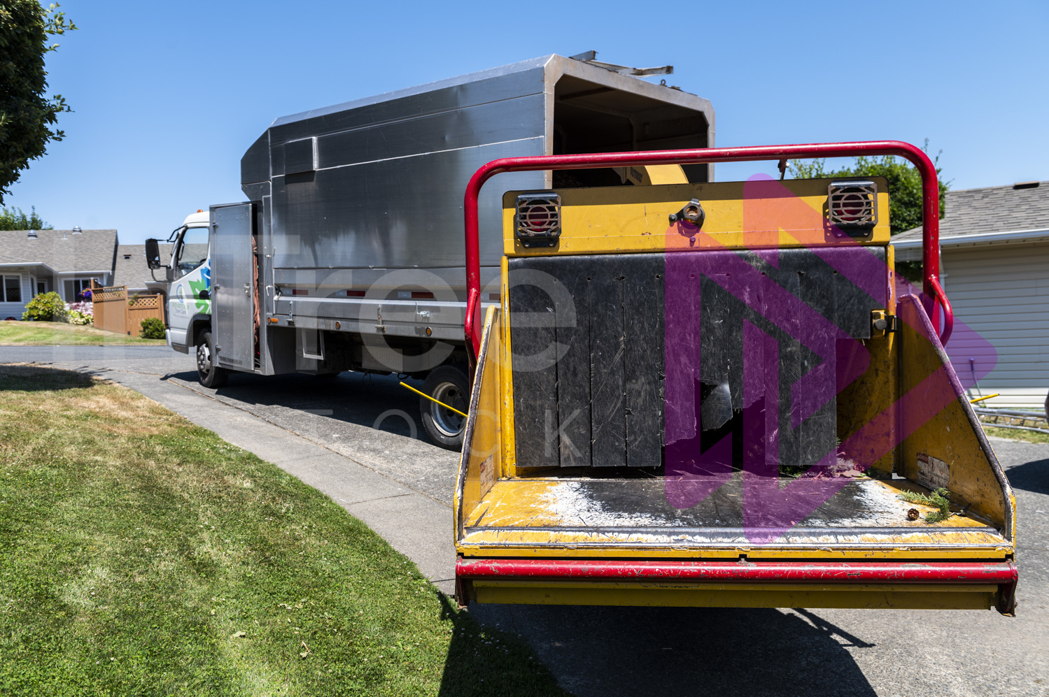 Yellow chipper and chip truck parked on residential driveway on a sunny day