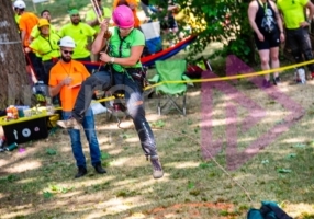 woman wearing pink protective helmet rappels out of a tree on a rope and climbing system