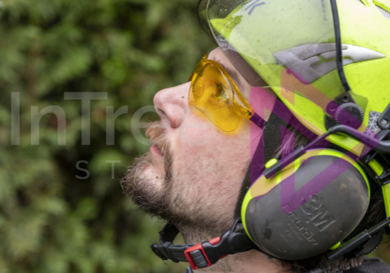 Close up of man wearing yellow safety glasses and a hi-viz green helmet with ear protection