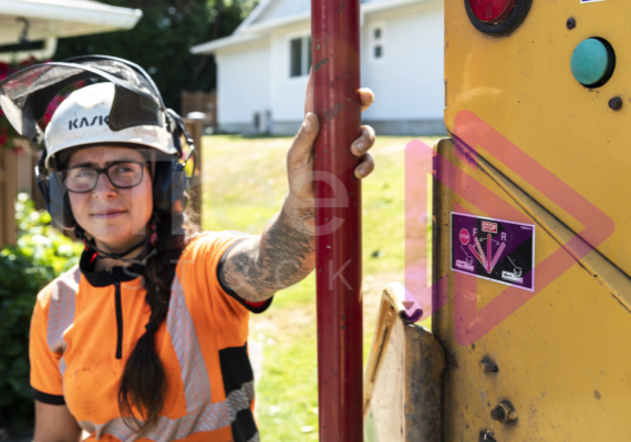 Female arborist pushing red stop bar with her hand on chipper