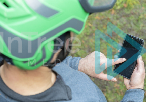 Male arborist in green helmet using smart phone in hand