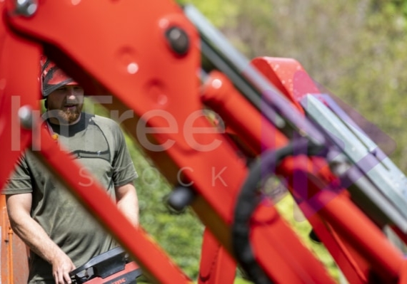 Man with remote control Looking through spider lift legs to man extending outriggers with remote control
