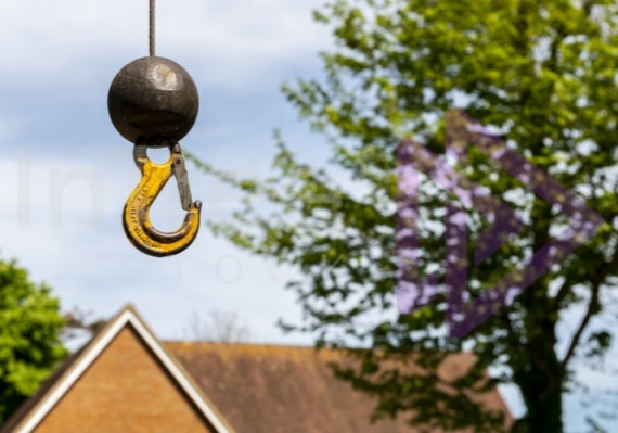 Small load crane ball and hook floating in air with tree and UK home blurred in background