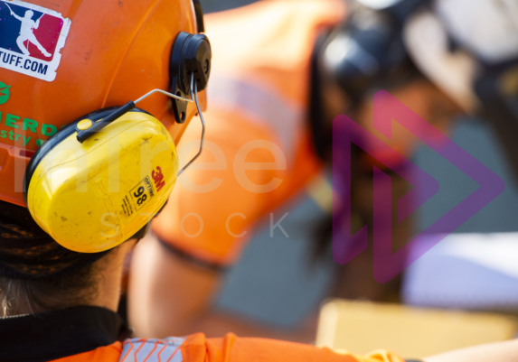 Yellow 3M Ear defender on helmet with woman blurred in background - Arborist Stock Photo-001-21-6274 Yellow 3M Ear defender on helmet with woman blurred in background