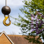 Small load crane ball and hook floating in air with tree and UK home blurred in background