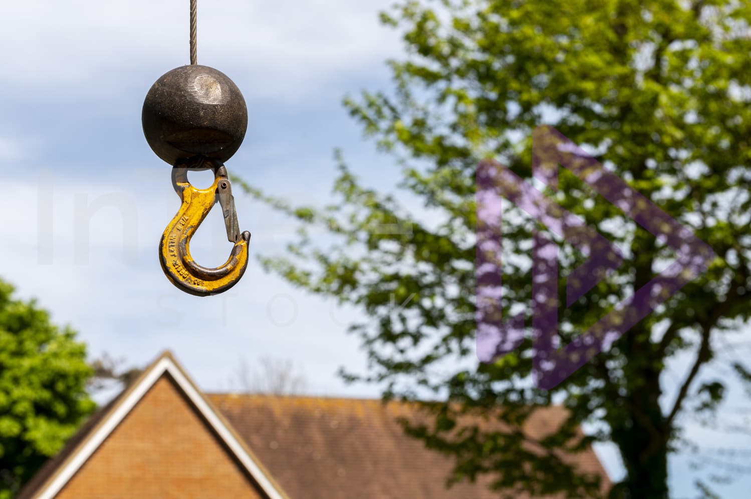 Small load crane ball and hook floating in air with tree and UK home blurred in background